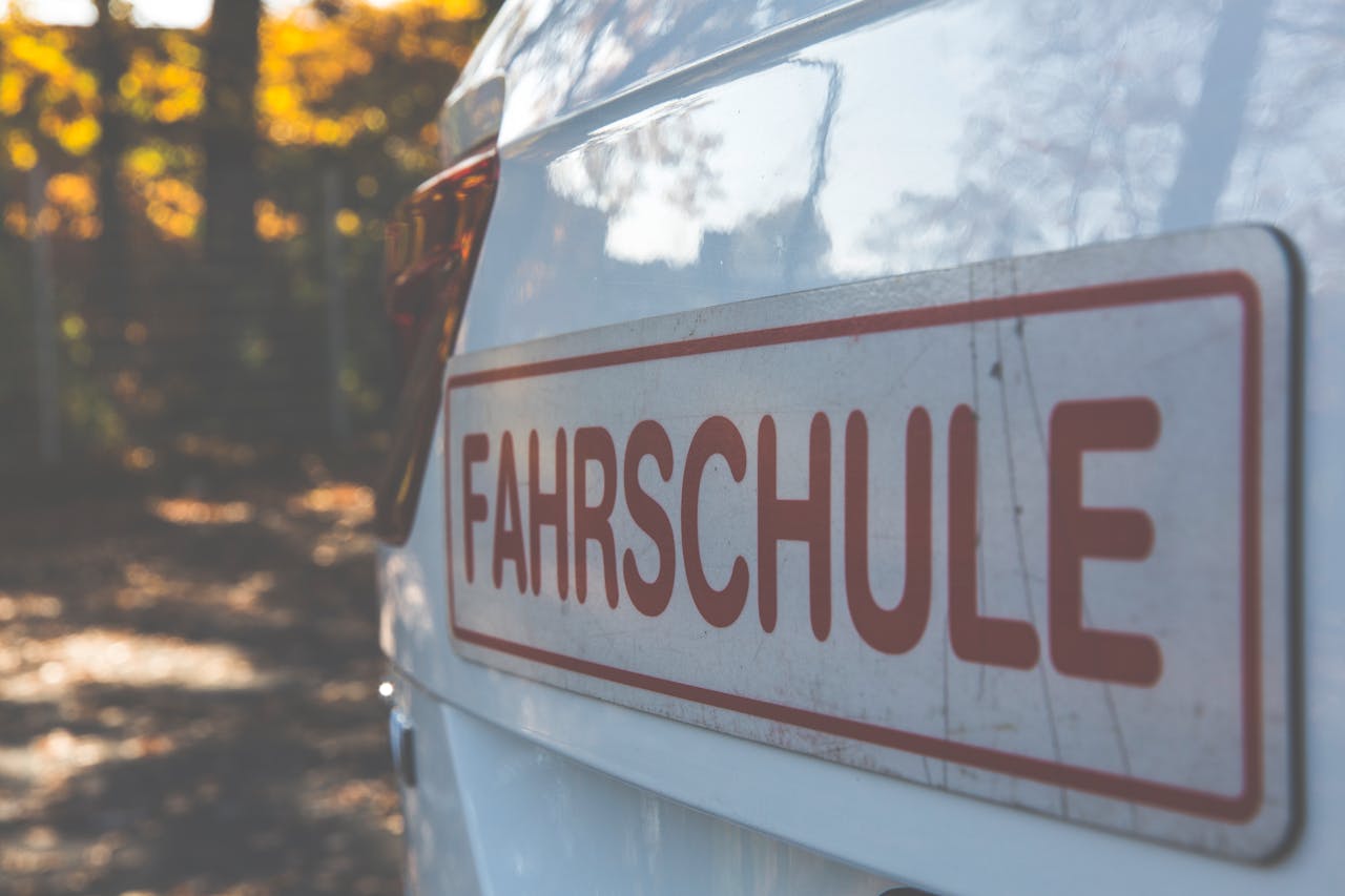 services-02 A side view of a white car with a Fahrschule sign, outdoors with autumn foliage.