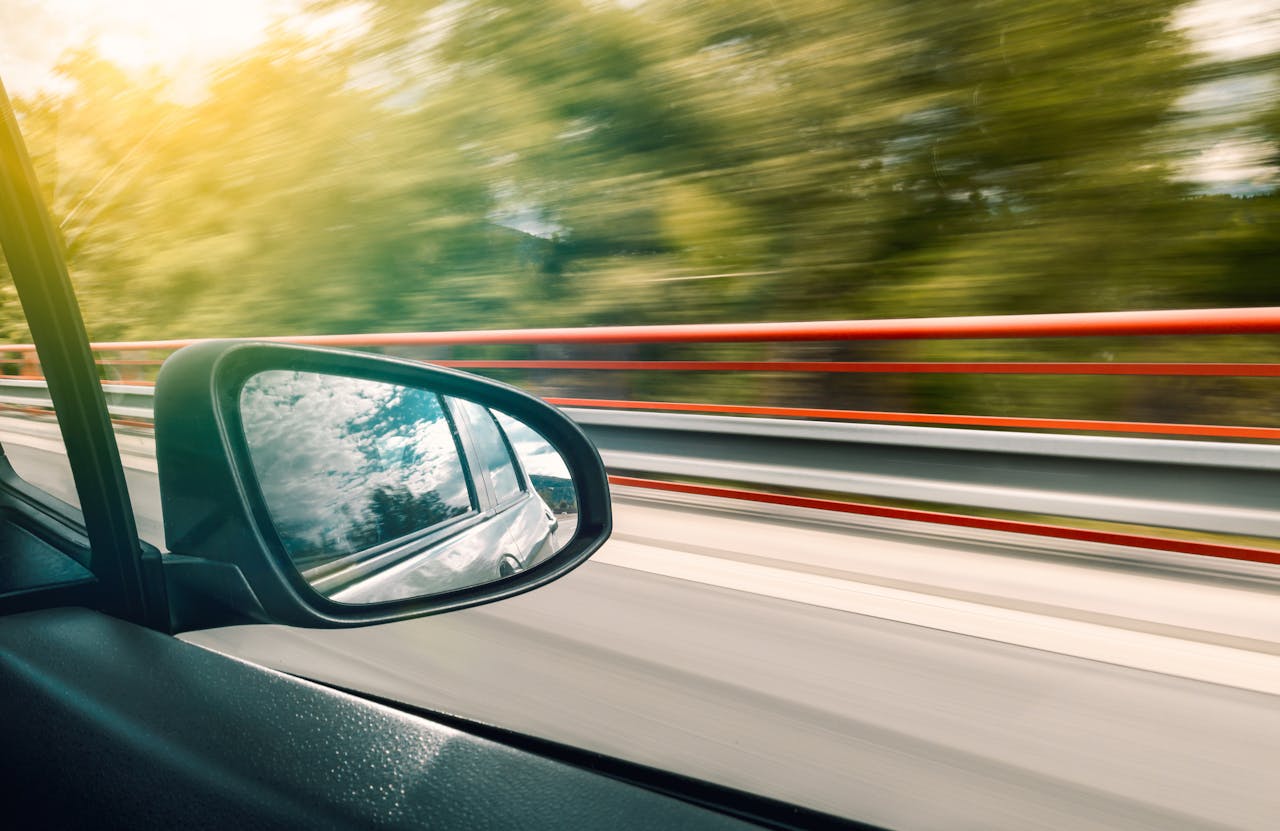team-01 Side mirror view capturing high-speed travel on an expressway with motion blur effect.